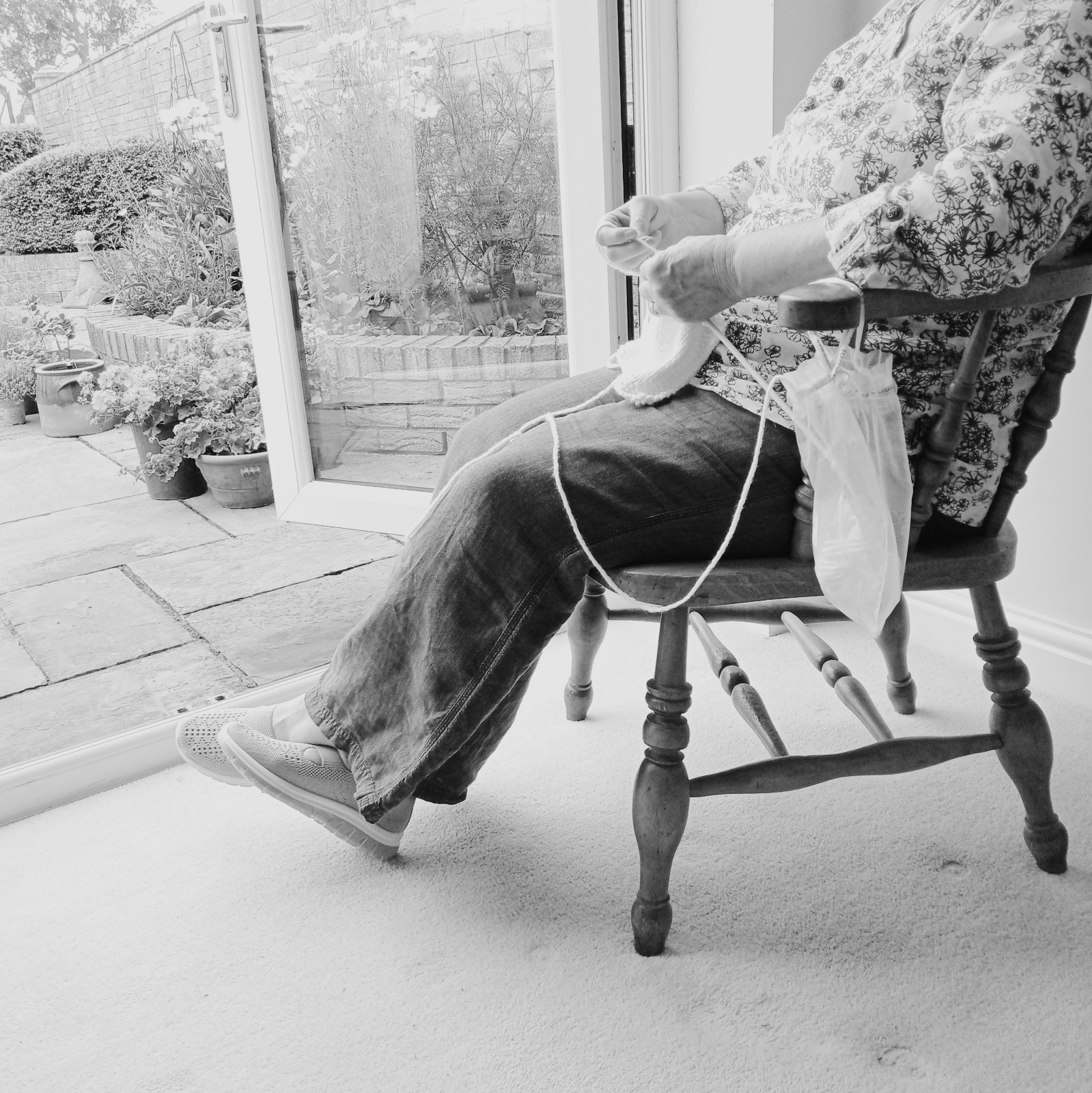 Bottom half of a person sitting in a chair handknitting a SKIN WISDOM® REVIVAL KNIT